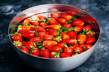 Strawberries in the water. Fresh strawberries in a bowl with water on a dark background. Summer and food art concept.