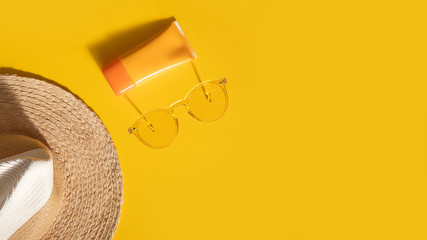 Sun protection objects. Straw woman's hat with sunglasses and protection spf cream top view on bright yellow background. Beach accessory. Summer Travel Vacation Concept. Sale kit. Copy space.