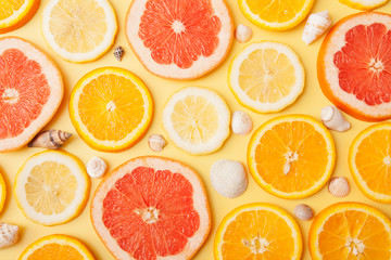 Flat lay slices of orange, grapefruit and lemon with shells on a yellow background. Summer citrus pattern