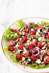 Salad with berries-raspberry, blueberry, sweet cherry, red onion, feta cheese, pine nuts . Dressed with raspberry vinaigrette. Soft focus.