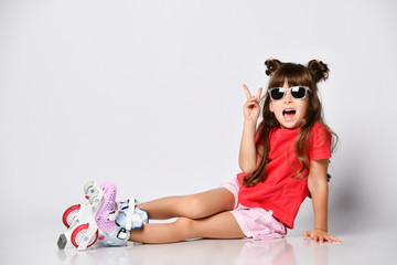 Beautiful girl posing sitting on the floor, in a red t-shirt and shorts and a fashionable hairstyle, in roller skates on her feet