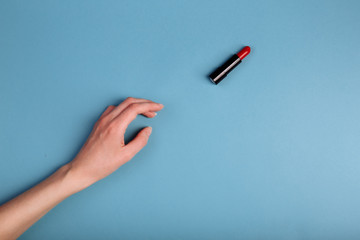 The woman's hand is taking red lipstick. isolated On the blue background