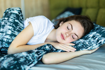 Young woman resting in bed with hands beside her head on the pillow.