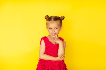 Pretty little barefooted girl with two buns and in bright pink summer dress posing with emotions on yellow background. Copy space