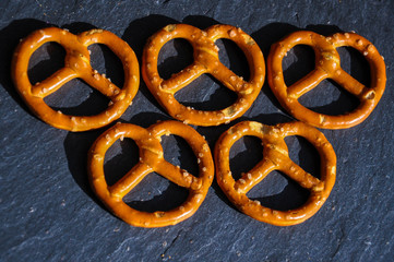 Top view of salted German mini pretzels in the shape of symbolic rings on the sunlit black stone background. Traditional German beer snack.