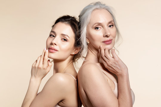 Elderly and young women with smooth skin and natural makeup standing back-to-back. 