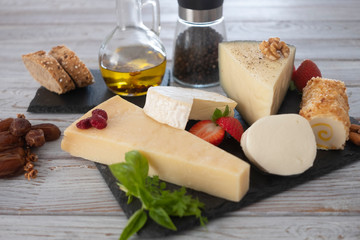 Assortment of cheese slices with fruits pepper and olive oil on wooden table