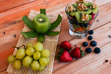 Fresh seasonal fruit salad in a glass on wooden rustic table. Healthy nutrition with papaya, kiwi, banana, strawberry, blueberry, walnuts and white grape