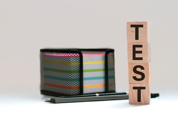 Wooden blocks spell out TEST on a blue bubble or scantron sheet with a number two yellow pencil.