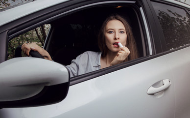 Young woman driving a car. The girl paints her lips in the car. Woman doing makeup in the car.