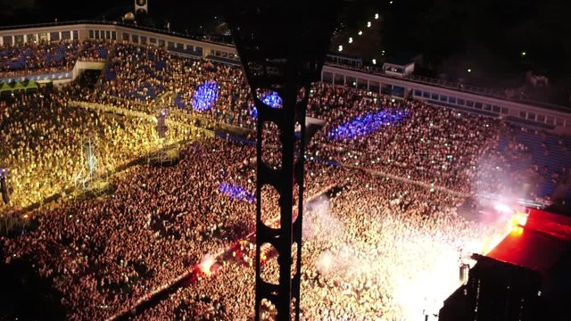 Aerial drone flight view of night show at stadium in Kiev. Bright spotlights blink with multi-colored light beams. Loud concert music and crazy party atmosphere in capital city centre. Huge croud danc