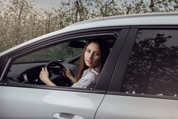 Young woman driving a car. The girl sits in the driver's seat. Young beautiful girl with a nice smile driving a car. Exterior view of the car