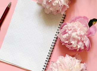 Notebook, pen and peonies flowers on a pink background. Top view. Copy space for text. Feminine concept.