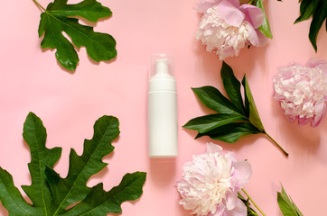 White bottle with place for your text on a pink background with flowers and leaves. Beauty concept.