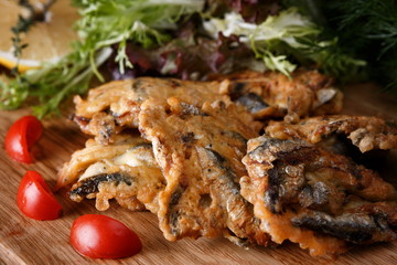 Fried fish sprat in batter, on a wooden board, with herbs, tomato and lemon