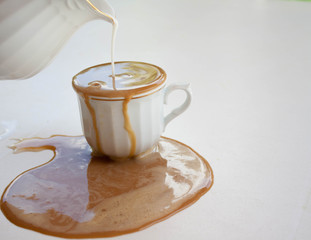 Café con leche en una taza blanca que se derrama sobre la mesa blanca.