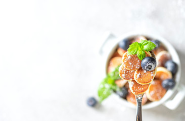 Pancake porridge. Mini pancakes on a spoon on a light concrete background. Trendy food mini pancakes.