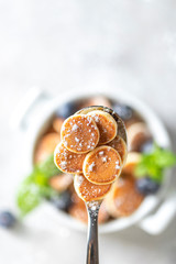 Pancake porridge. Mini pancakes on a spoon on a light concrete background. Trendy food mini pancakes.