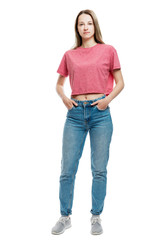 Fototapeta premium A young girl in jeans and a red T-shirt stands holding hands in pockets. Full height. Isolated on a white background. Vertical.