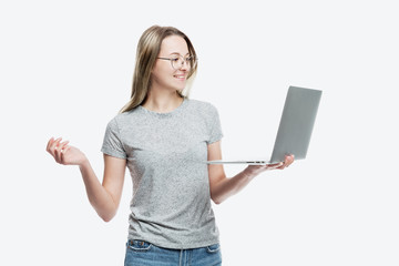 A smiling young girl in glasses stands with a laptop in her hands. Education, work and blogging. Isolated on a white background.