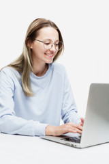 A smiling young girl in glasses stands with a laptop in her hands. Education, work and blogging. Isolated on a white background. Vertical.