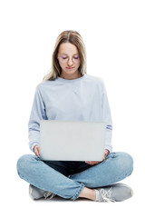 A smiling young girl in glasses sits with a laptop in her hands. Education, work and blogging. Isolated on a white background. Vertical.