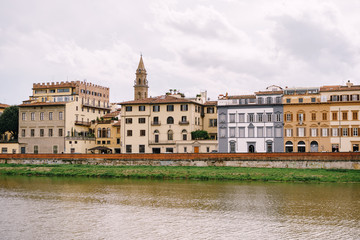 Fototapeta na wymiar Houses on the waterfront in Florence, Italy, on the Arno River. The bell tower of basilica of Santo Spirito.