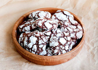 Cracked chocolate cookies sprinkled with icing sugar in a wooden plate. Chocolate christmas cookies.