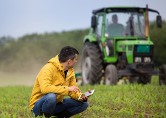 Farmer with tablet in field with tractor in background