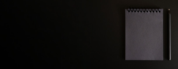 notebook on a spring with black sheets and a pen on a black background. space for text. banner