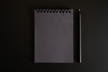 notebook on a spring with black sheets and a pen on a black background. space for text