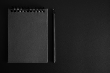 notebook on a spring with black sheets and a pen on a black background. space for text