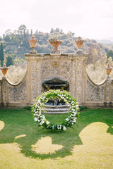 Wedding at an old winery villa in Tuscany, Italy. Round wedding arch decorated with white flowers and greenery in front of an ancient Italian architecture.