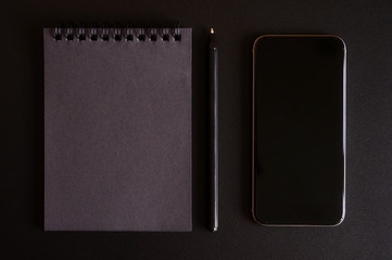 notebook on a spring with black sheets, and a pen, and mobile phone on a black background. space for text