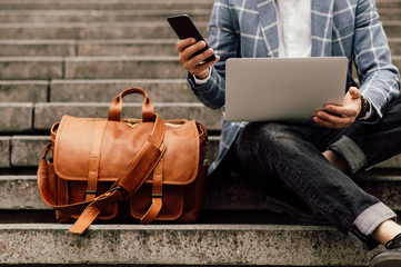  businessman sits on a shoe with laptop and brown leather bag