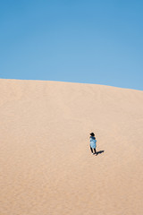 A travel girl is running on the top of a sand dune back to the camera. A traveler in a black hat and blue skirt in Death Valley National Park