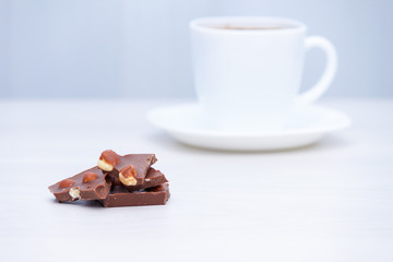 Cup of coffee with milk chocolate with nuts on white wooden table.