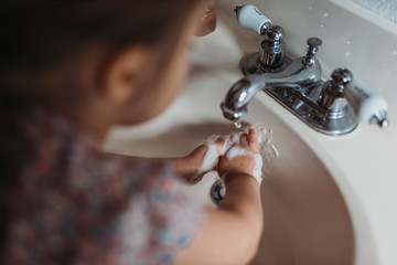 Young preschool aged girl washing hands in sink with soap