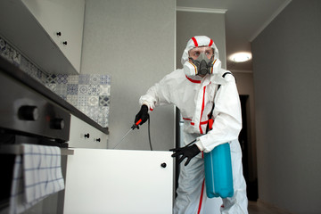 pest control. A worker in a protective suit cleans the shelves in the kitchen from cockroaches with...
