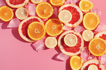Close up cut slice of orange, grapefruit, lemon fruits and ice on pink background  with hard light, copy space. Summer and cooling freshness concept. Cold food at hot weather. Making juice.