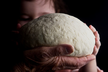 Grandmother makes bread with a small child close-up. The dough in the old wrinkled palms of the good grandmother in the dark. Grandmother with bread close-up