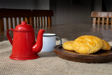 corn bread on wooden plate, with red teapot and white cup on table
