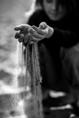 a thoughtful little girl drops sand through her fingers sitting on the beach. Kid girl having fun in holiday vacation. Black and white photo.