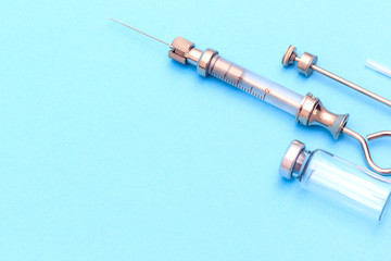 antique syringe and a glass ampoule next to it on a blue background. next to the parts from the syringe