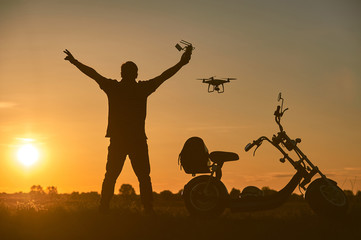 Fototapeta na wymiar The flying drone pilot controls the drone in the rays of the setting sun. Nearby is an electric scooter.
