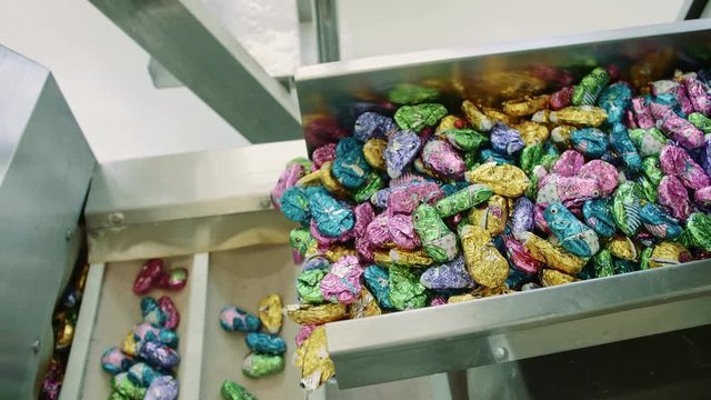 Candy factory. Sweets spilling from conveyor. Bunch of wrapped candies falling from conveyor on packing containers in confectionery factory. 4K