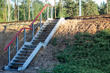 Stairs made of concrete and metal across the railway tracks. Crossing rails in a forest and field