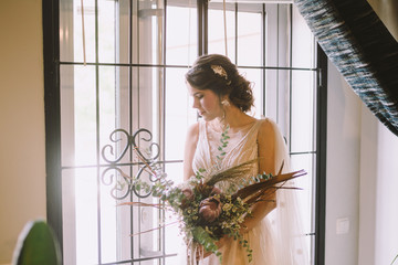 Elegant morning photo. Wedding. Bride. Preparation. Bride with a bouquet of flowers near the window. Wedding in European style. Morning bride waiting for the groom on the wedding day