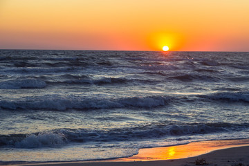 An orange sunset evening over the Black sea with big dark waves, Kinburn Foreland shore, Ukraine