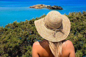 Young woman with straw hat looking at the sea.